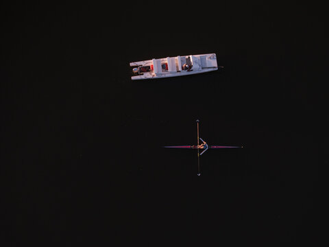 Aerial view of a lone boat and a rower cutting through the dark, still waters of the Charles River, Boston, Massachusetts, United States.