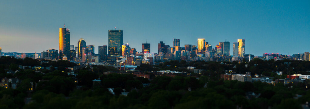 Aerial view of the gleaming Boston skyline, bathed in the warm glow of the setting sun, stands tall against the twilight sky, Boston, Massachusetts, United States.