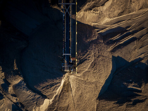 Aerial view of a conveyor belt system contrasting with the textured earth and shadows, creating a stark industrial landscape, Boston, Massachusetts, United States.