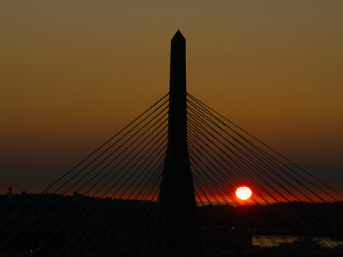 Aerial view of the Zakim Bridge silhouetted against a fiery sunset, its cables like harp strings in the twilight, Boston, Massachusetts, United States.