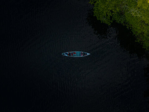Aerial view of a lone canoe cuts through the inky waters of the Charles River, framed by lush green foliage, Boston, Massachusetts, United States.
