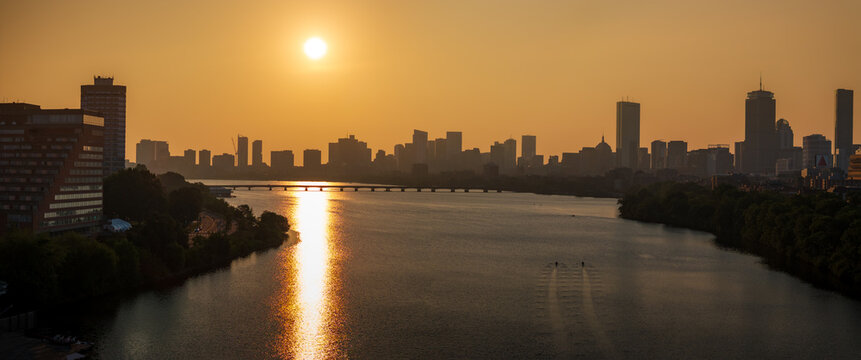 Aerial view of Boston's skyline silhouetted against a fiery sunset, with the Charles River reflecting the sun's golden rays, Boston, Massachusetts, United States.