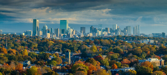 Aerial view of Boston's skyline rises majestically beyond a vibrant tapestry of autumnal foliage, painting a stunning contrast against the cloudy sky, Boston, Massachusetts, United States.