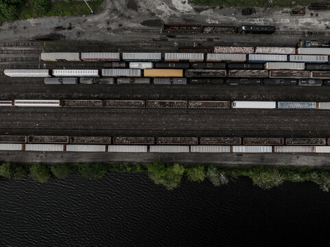 Aerial view of freight train cars lined up on tracks alongside the dark waters, a stark contrast of industrial grit and natural flow, Boston, Massachusetts, United States.