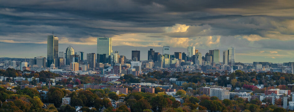 Aerial view of Boston's skyline under a moody sky, where skyscrapers pierce the horizon amidst the changing autumn foliage, Boston, Massachusetts, United States.