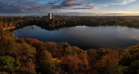 Aerial view of a tranquil lake mirroring the sky, framed by vibrant autumn foliage, with the city skyline in the distance, Boston, Massachusetts, United States.