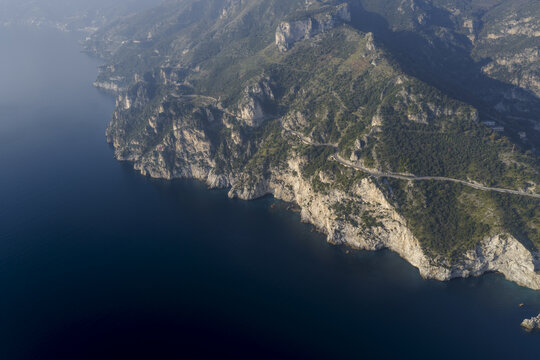 Aerial view of rugged cliffs embrace the azure sea, where a winding road snakes along the dramatic coastline, Erchie, Amalfi Coast, Campania, Italy.