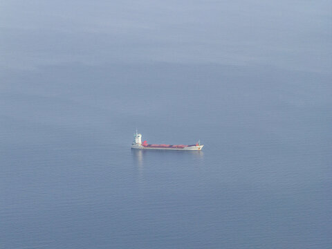Aerial view of a cargo ship cuts through the serene blue expanse of the sea, contrasting against the vast horizon, Erchie, Amalfi Coast, Campania, Italy.