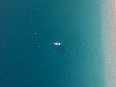 Aerial view of a lone white boat adrift on the vast expanse of turquoise waters, contrasting with the sandy shoreline, Erchie, Amalfi Coast, Italy.