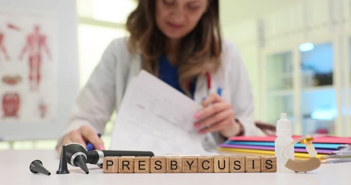 Wooden blocks spell word Presbycusis near ear model and hearing aids. Woman doctor writes notes about hearing loss planning tests for patient