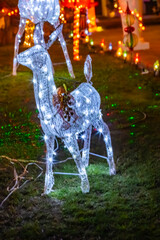 A statue of a white Christmas reindeer made of light bulbs stands in a night garden.
