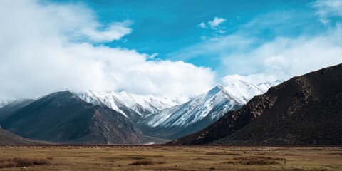 Snow-capped mountain range under clear blue sky with rolling hills