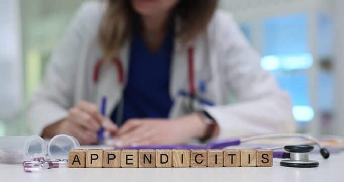 Wooden blocks spell word Appendicitis near pills and stethoscope. Woman doctor writes diagnosis report noting strong abdominal pain signs in patient