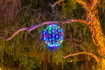 A decorative ball with blue and purple lights hangs on the tree.

