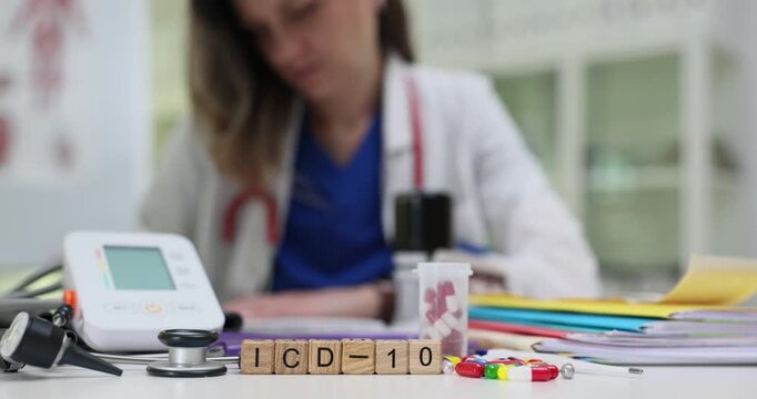 Wooden blocks spell code ICD 10 near blood presure monitor and stethoscope. Woman doctor enters diagnosis code organizing patient medical records