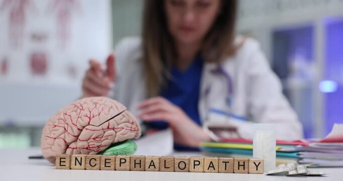 Wooden blocks spell word Encephalopathy in front of brain model. Woman doctor studies cognitive decline symptoms writing patient neurological report
