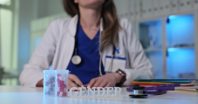 White letters on stand spell word Gender near pills containers. Woman doctor writes research notes about identity topics and health outcomes