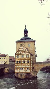 Picturesque old town hall, a medieval building constructed in the middle of the regnitz river, a famous landmark of bamberg, germany on an overcast day with the water flowing beneath it