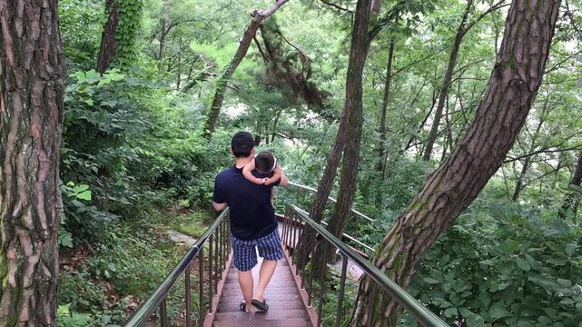아빠가 아기를 안고 울창한 숲속 계단을 내려오는 모습