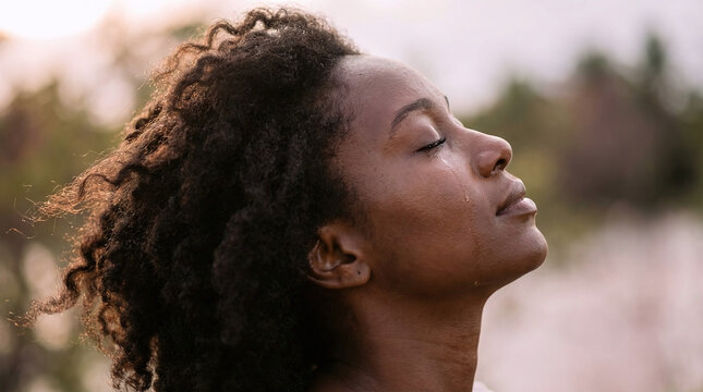 Portrait de profil d'une femme en pri&egrave;re, les yeux ferm&eacute;s, laissant couler une larme sur sa joue, en ext&eacute;rieur