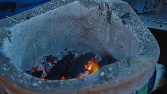 lose-up of burning red charcoal inside an old-style clay stove used for authentic street food cooking.