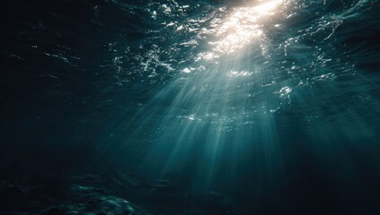 Underwater view looking up at sunbeams penetrating dark blue water surface