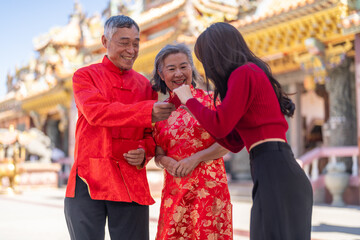 Obraz premium Asian girl happy receiving red envelope from grandparents in traditional chinese clothes, celebrating lunar new year at ornate temple, joyful family moment, culture and love shared between generations