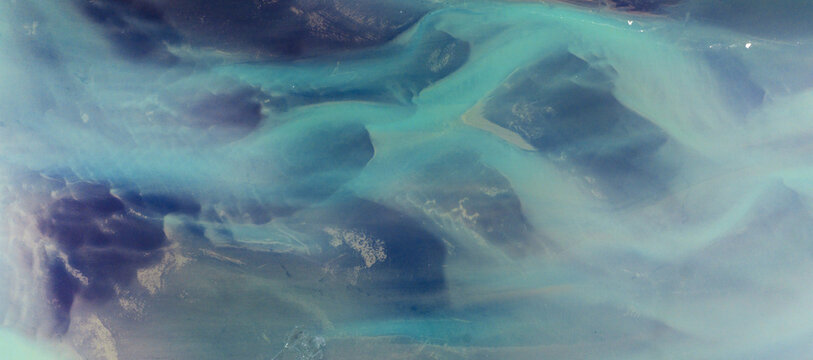 Aerial view of glacial river braiding through a stark landscape, teal waters weaving intricate patterns against the dark earth, Hafnarfjordur, Hafnarfjardarkaupstadur, Iceland.
