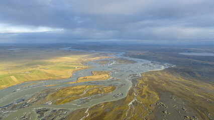 Aerial view of braided rivers carving through a stark landscape under a vast sky, creating a symphony of grey, beige, and brown hues, Iceland, ICELAND.
