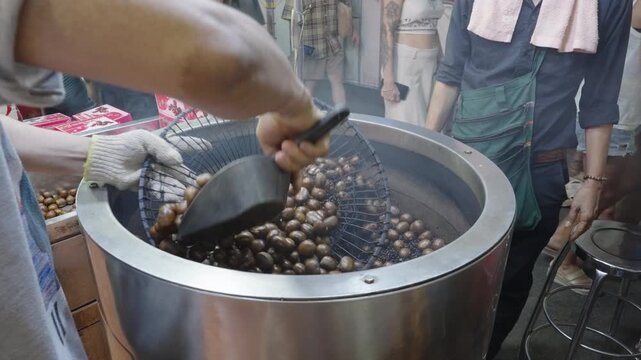 Vendor stirring chestnuts (Kao Luck) in heated black coffee beans or sand to roast them evenly. Yaowarat Road, Bangkok.