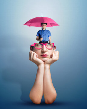 Portrait of a thoughtful woman in glasses with a small copy of herself with an umbrella visible from her head. Concept of protection, mental health, self-help, or inner critic, voices in the head