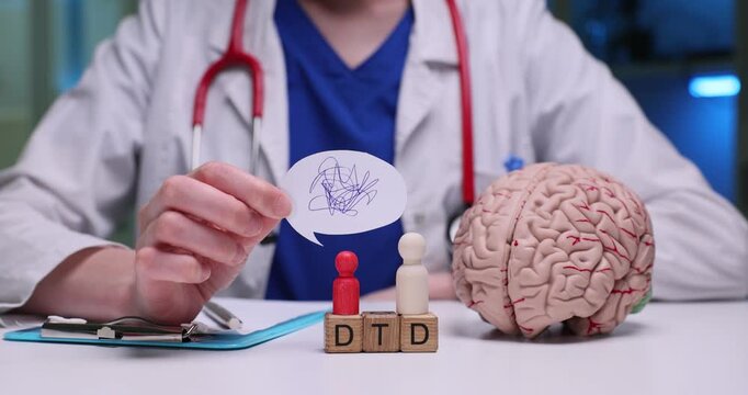 Doctor sits calmly at desk during routine patient consultation. Neatly arranged wooden cubes form abbreviation DTD near anatomical brain model