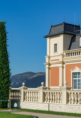 Classical building of Chateau de Talyu winery with decorative balustrade and tower under blue sky against majestic mountains rise, adding to scenic beauty. Gelendzhik, Russia - September 30, 2024