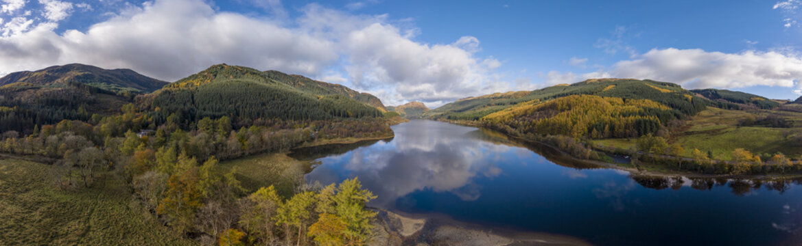 Aerial view of Loch Lubnaig's tranquil, dark waters mirroring the sky and surrounding hills blanketed in autumn's gold and green hues, Callander, Scotland, United Kingdom.