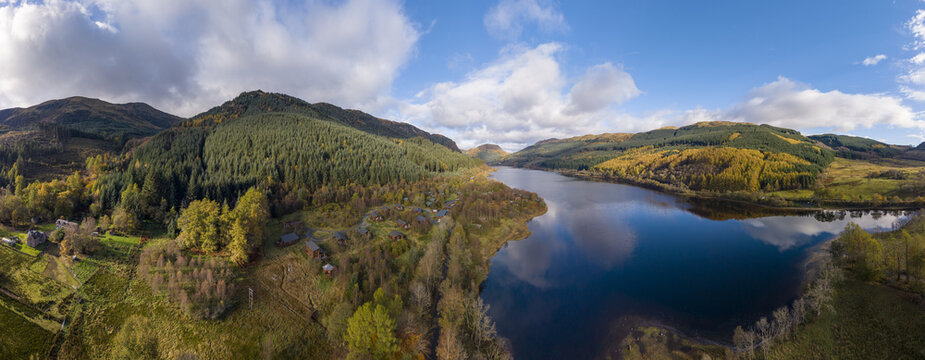 Aerial view of the dark waters reflecting the sky, embraced by forests and mountains ablaze with autumn colors, Callander, Scotland, United Kingdom.