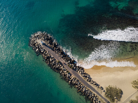 Aerial view of a rocky breakwater extending into the turquoise sea, waves crashing against the shore, Mooloolaba, Queensland, Australia.