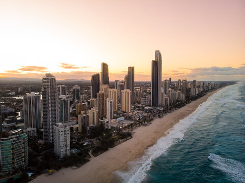 Aerial view of the golden beach kissed by foamy waves beside towering skyscrapers under the soft glow of dawn, Surfers Paradise, Queensland, Australia.