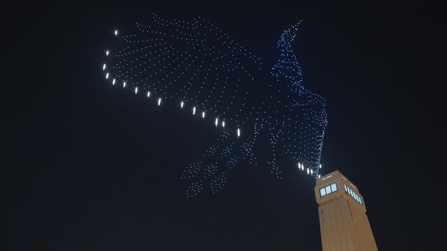 Hundreds of synchronized drones forming artistic patterns with LED lights against the dark night sky during a celebration in Thailand's capital.