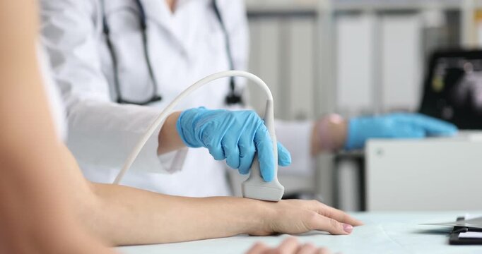 Medical worker in gloves presses ultrasound probe on female forearm and wrist. Specialist scans blood vessels on monitor checking circulation status