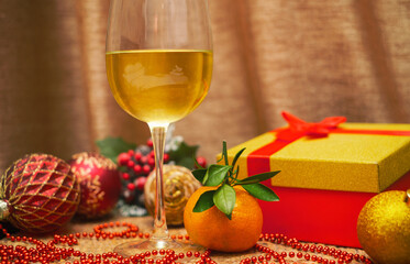 A glass of wine and a tangerine next to a gift in a box with Christmas tree balls