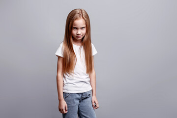 Moody angry young girl staring from under her brow, expressing hurt feelings, negative emotions while standing in studio, kids emotional portrait and facial expression on neutral background