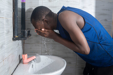 handsome man standing in a modern bathroom washing his face at the sink.