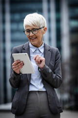 Senior business woman holds tablet and smiles in city area
