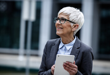 Senior business woman holds tablet and smiles in city area