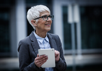 Senior business woman holds tablet and smiles in city area