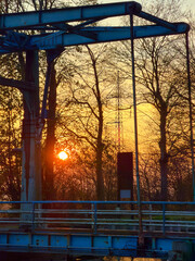 Rijkevorsel, Antwerpse Kempen, Belgium, Bridge silhouette at golden sunset glow, industrial steel structure with weathered railings framed by bare trees, warm orange