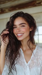 A woman with long hair is smiling and wearing a white shirt. She has a lot of hair and is posing for a picture