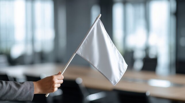 Negotiation Gesture: A hand holding a white flag in a conference room signifies a gesture of surrender, peace, or a desire for negotiation in the business landscape.