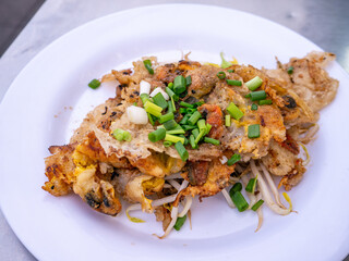 Crispy Thai Oyster Omelette (Hoi Tod) served with fresh bean sprouts and spring onions on a white plate