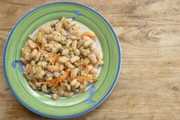 white bean salad with carrots and herbs on green plate close up
